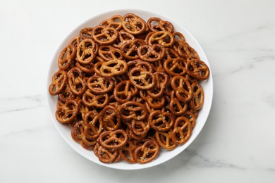 Photo of Tasty pretzel crackers in bowl on white marble table, top view