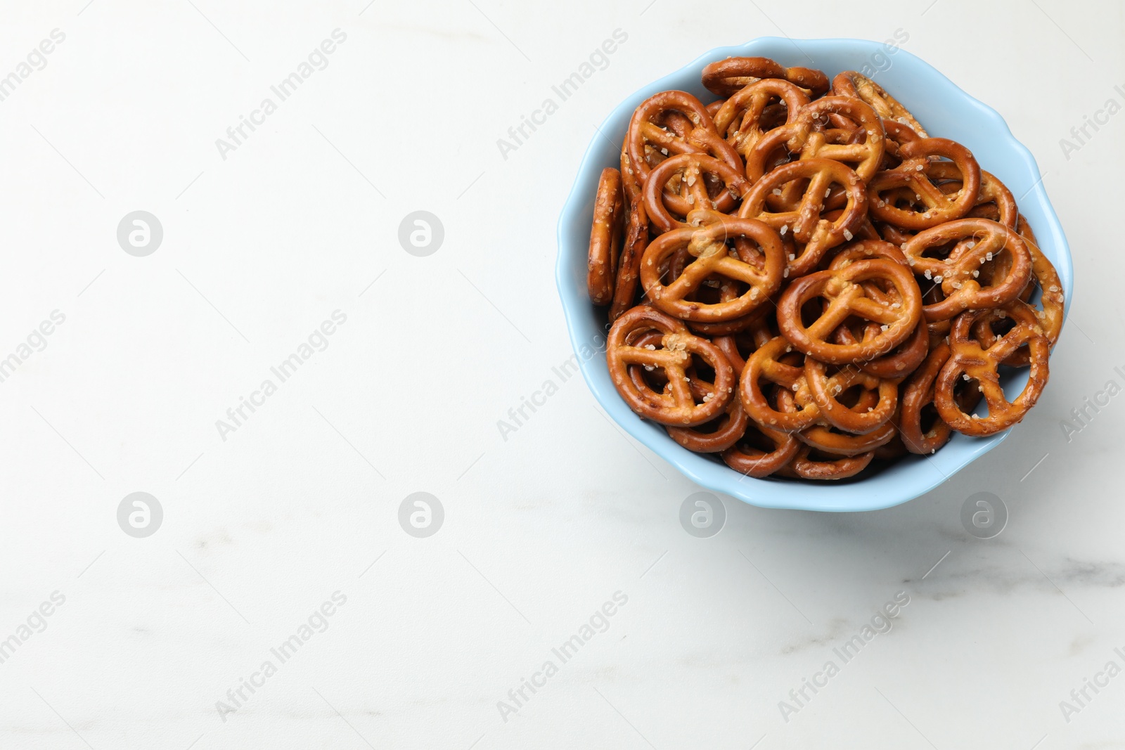 Photo of Tasty pretzel crackers in bowl on white marble table, top view. Space for text