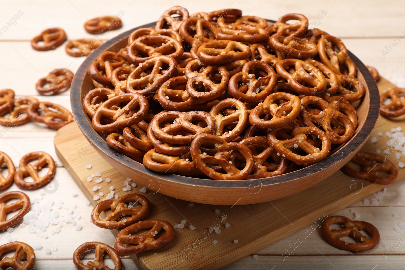 Photo of Tasty pretzel crackers with salt on light wooden table, closeup