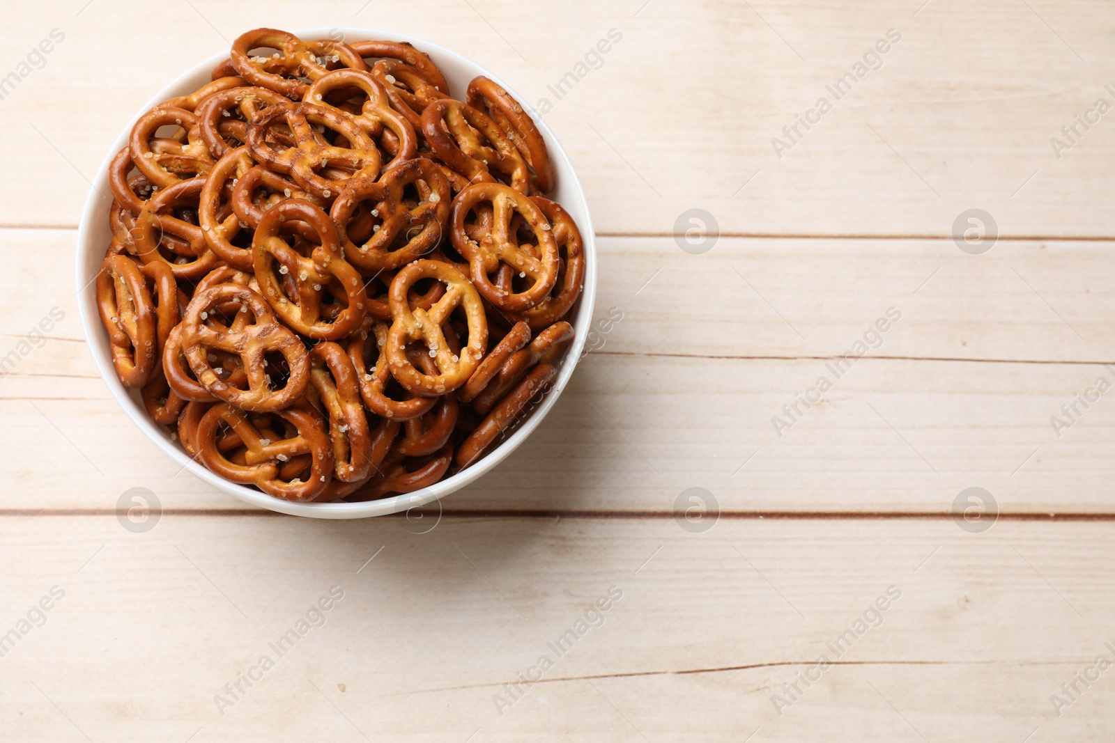 Photo of Tasty pretzel crackers in bowl on light wooden table, top view. Space for text