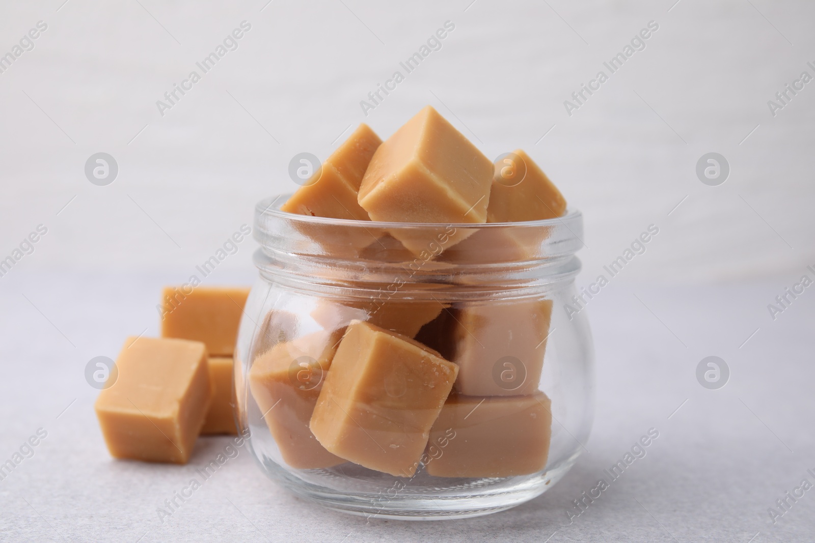 Photo of Tasty sweet caramel candies in glass jar on light table, closeup