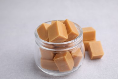 Photo of Tasty sweet caramel candies in glass jar on light table, closeup