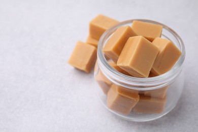 Photo of Tasty sweet caramel candies in glass jar on light table, closeup. Space for text