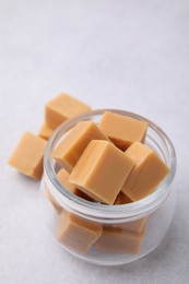 Photo of Tasty sweet caramel candies in glass jar on light table, closeup