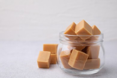 Photo of Tasty sweet caramel candies in glass jar on light table, space for text