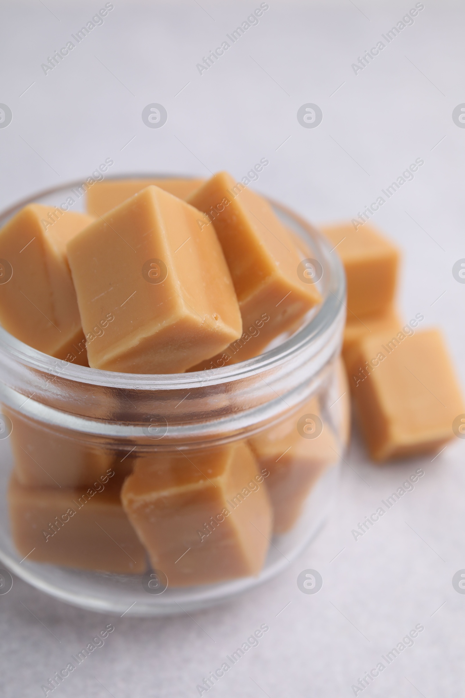 Photo of Tasty sweet caramel candies in glass jar on light table, closeup