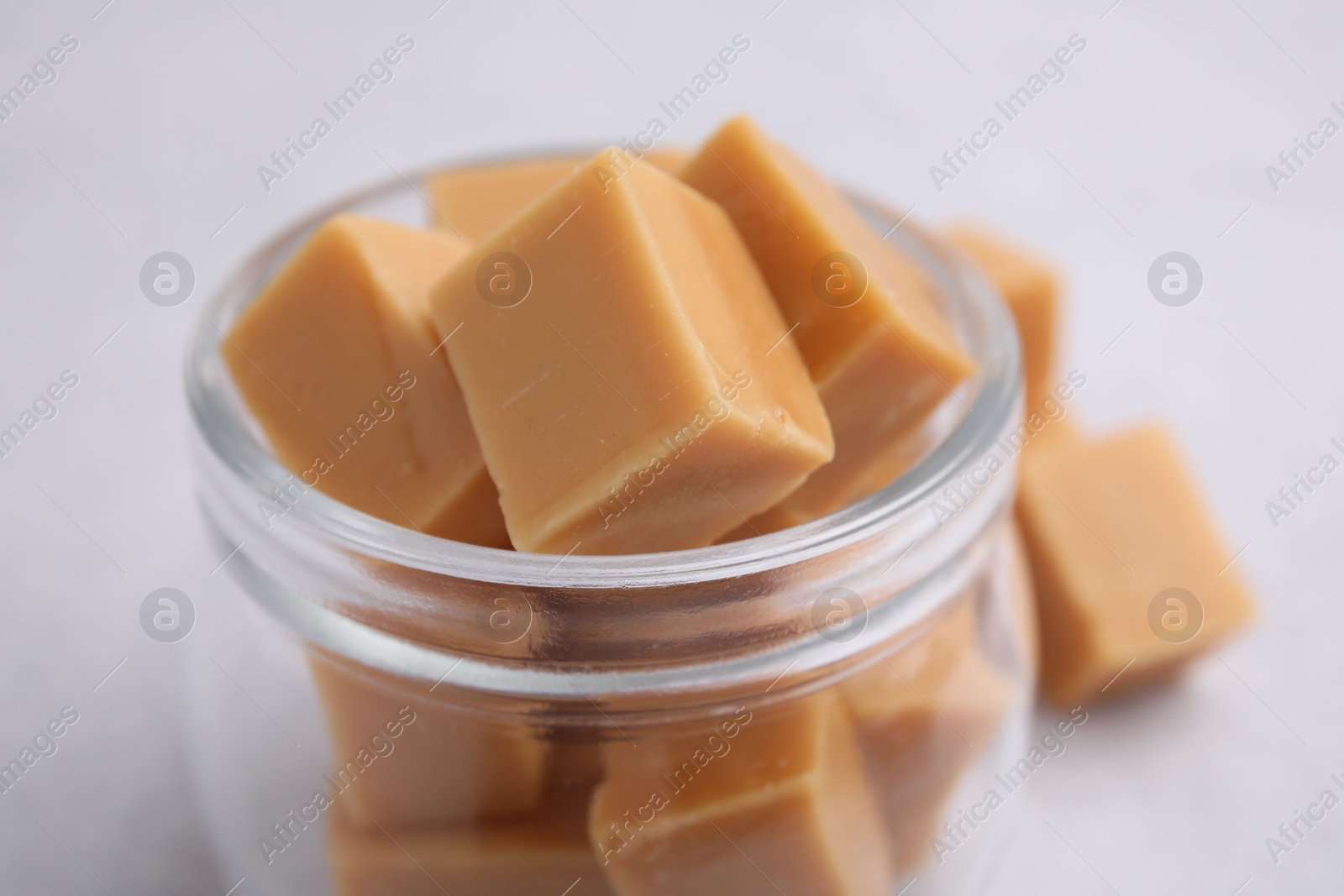 Photo of Tasty sweet caramel candies in glass jar on light table, closeup