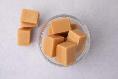 Photo of Tasty sweet caramel candies in glass jar on light table, top view