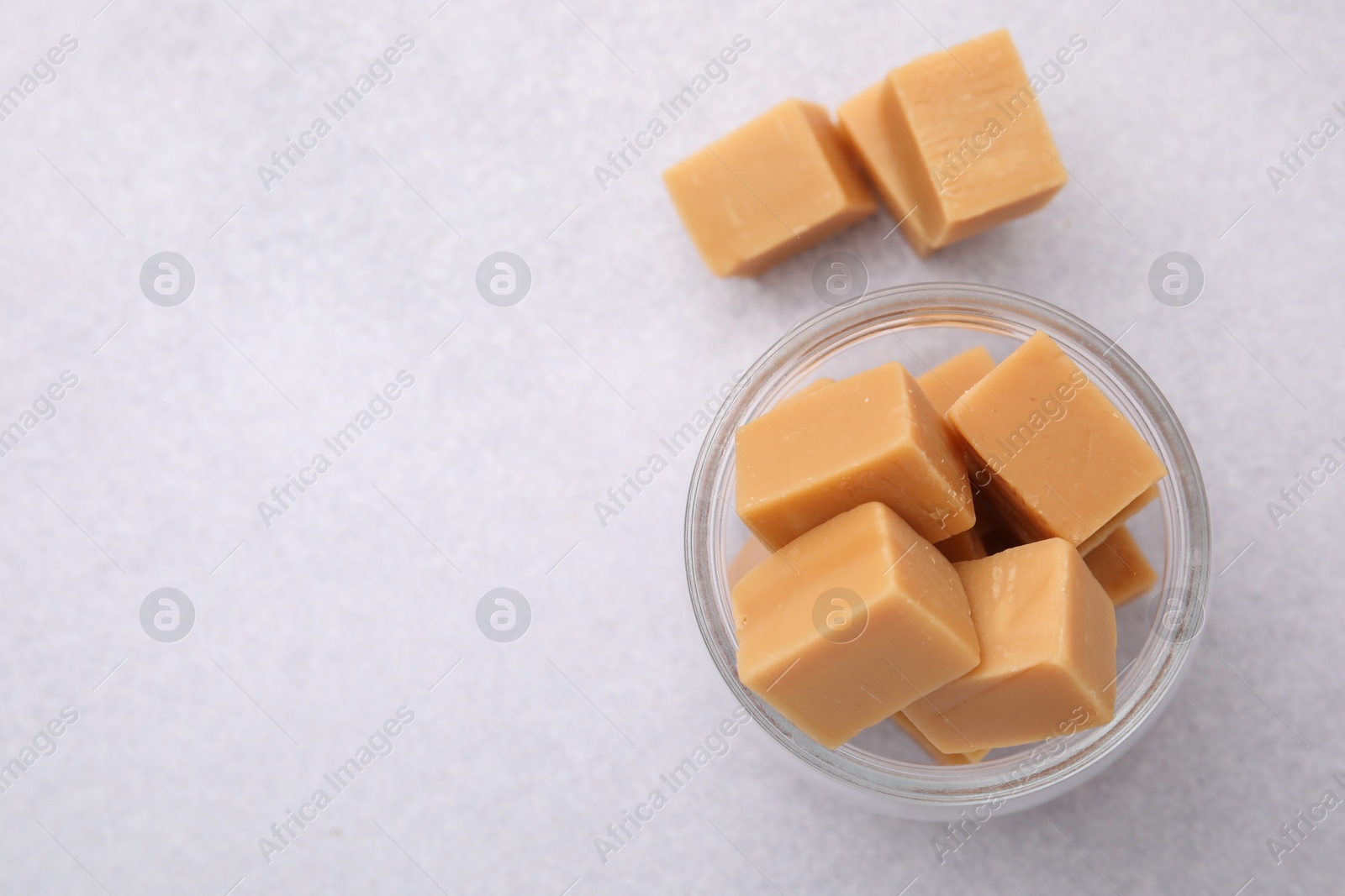 Photo of Tasty sweet caramel candies in glass jar on light table, top view. Space for text