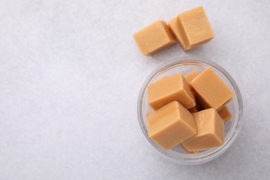 Photo of Tasty sweet caramel candies in glass jar on light table, top view. Space for text