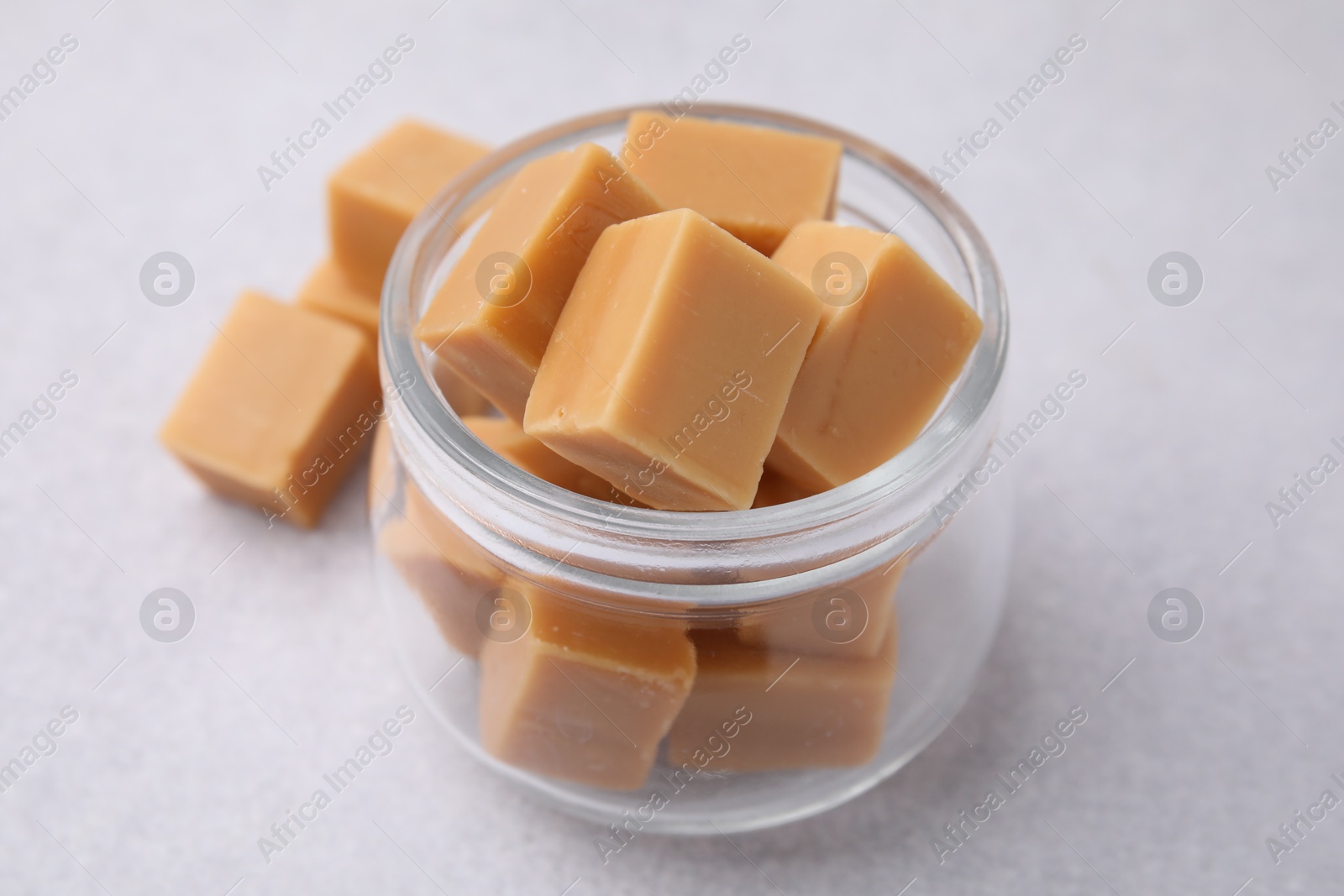 Photo of Tasty sweet caramel candies in glass jar on light table, closeup