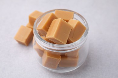 Photo of Tasty sweet caramel candies in glass jar on light table, closeup