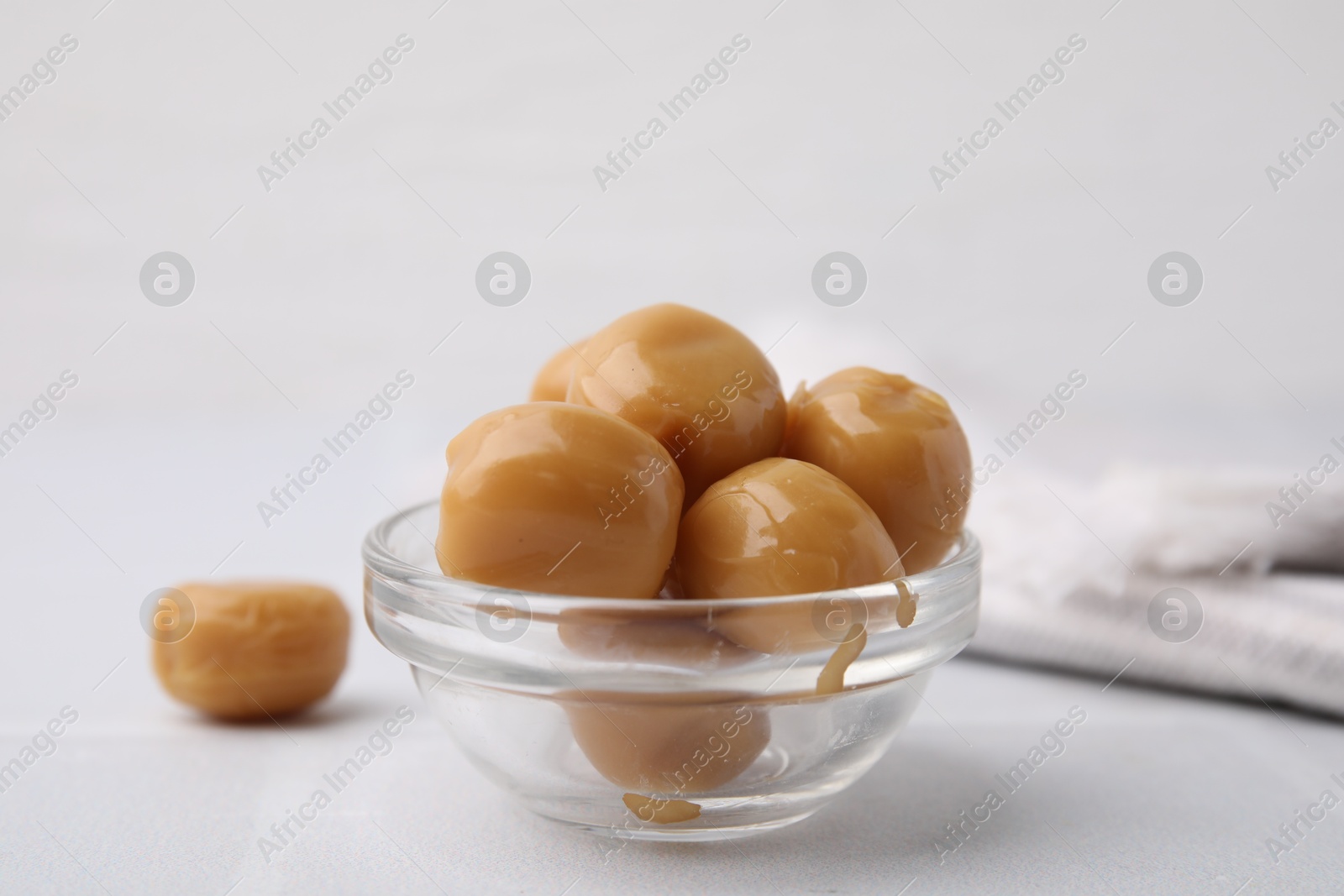 Photo of Tasty hard toffee candies in glass jar on light table, closeup