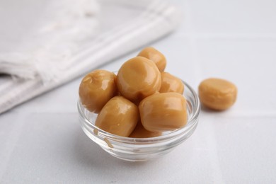 Photo of Tasty hard toffee candies in glass jar on light table, closeup