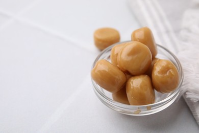 Photo of Tasty hard toffee candies in glass jar on light table, closeup. Space for text