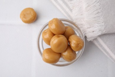 Photo of Tasty hard toffee candies in glass jar on light table, top view