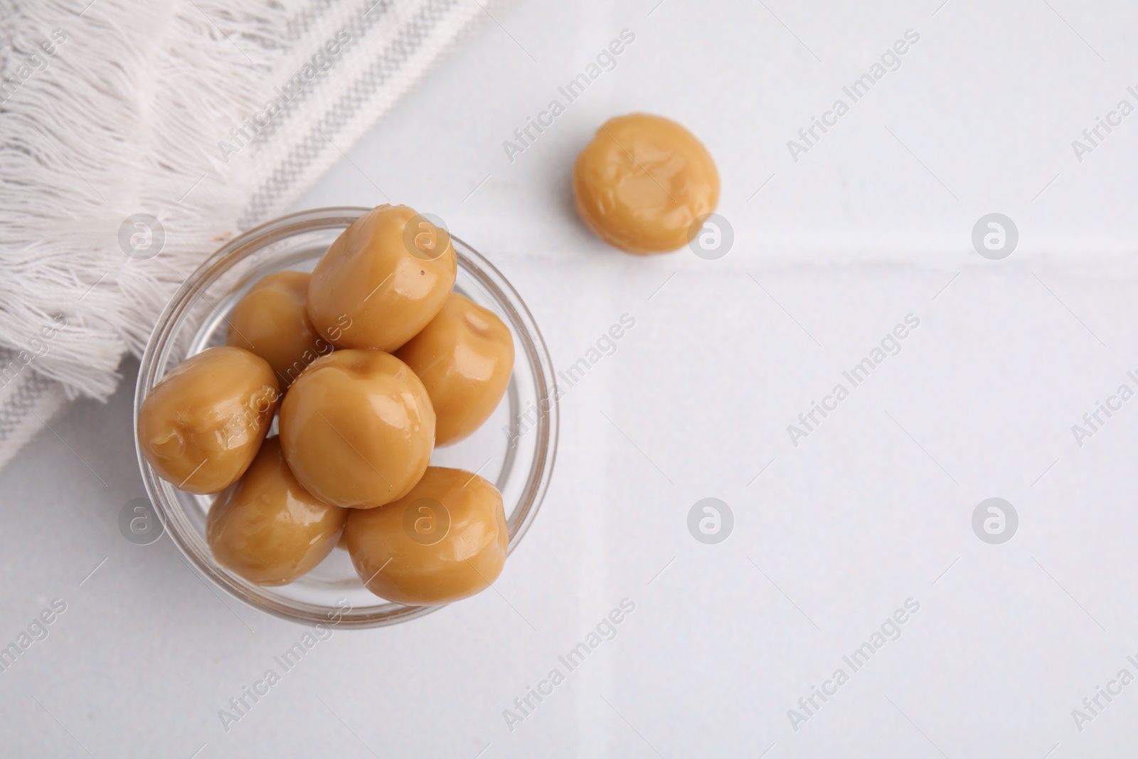 Photo of Tasty hard toffee candies in glass jar on light table, top view. Space for text