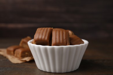 Photo of Tasty sweet caramel candies in bowl on wooden table, closeup