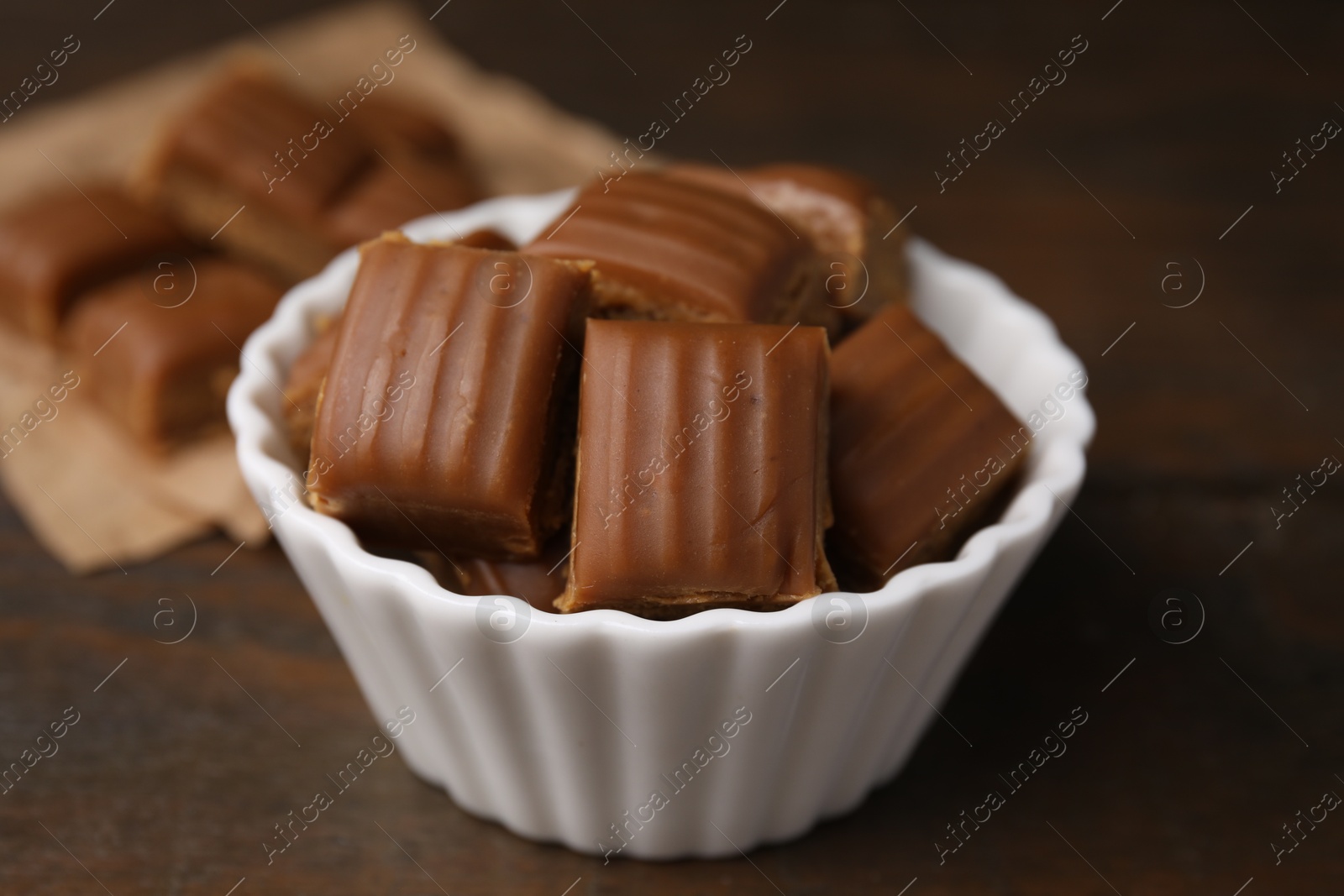 Photo of Tasty sweet caramel candies in bowl on wooden table, closeup