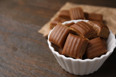 Photo of Tasty sweet caramel candies in bowl on wooden table, closeup. Space for text