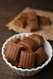 Photo of Tasty sweet caramel candies in bowl on wooden table, closeup