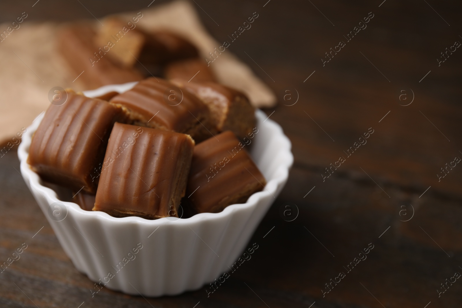 Photo of Tasty sweet caramel candies in bowl on wooden table, closeup