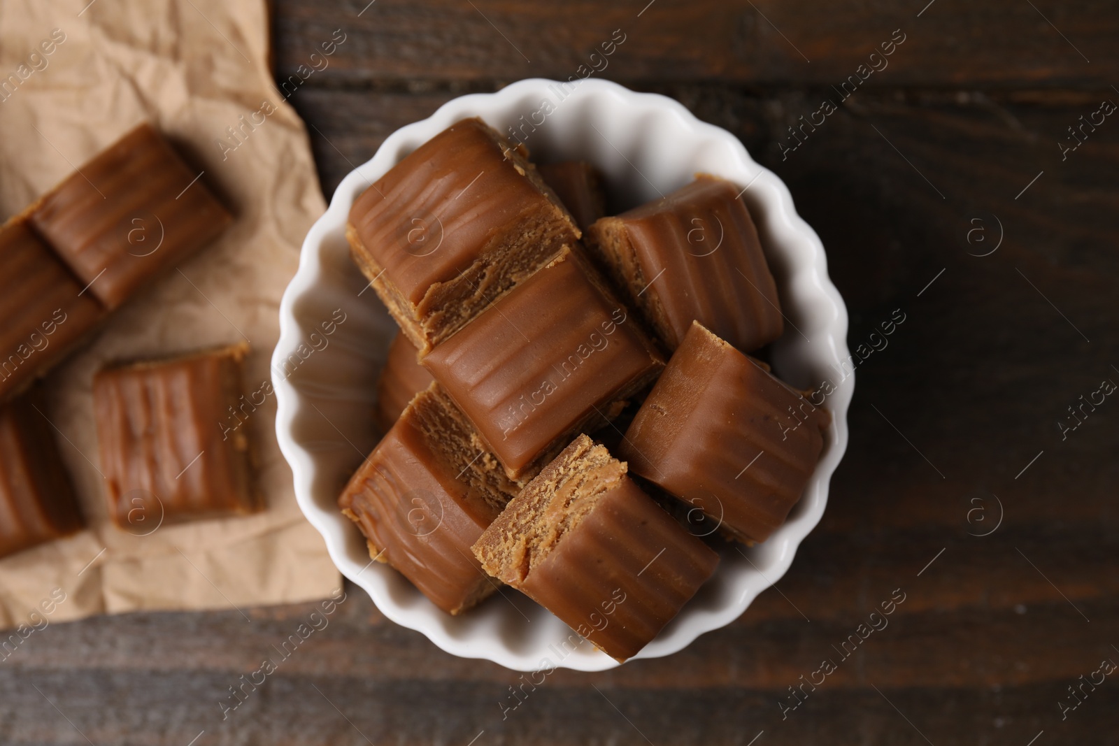 Photo of Tasty sweet caramel candies in bowl on wooden table, top view