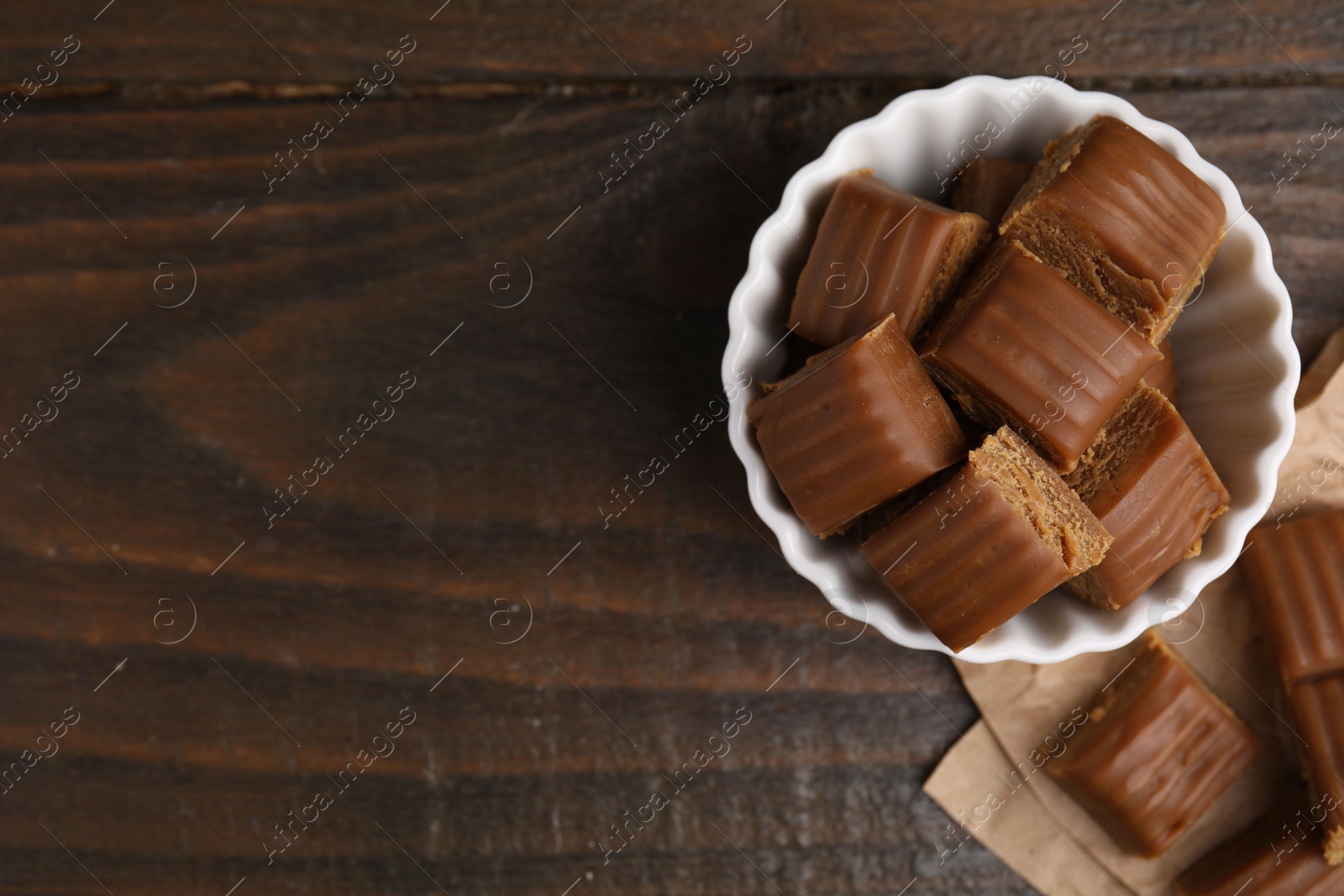 Photo of Tasty sweet caramel candies in bowl on wooden table, top view. Space for text