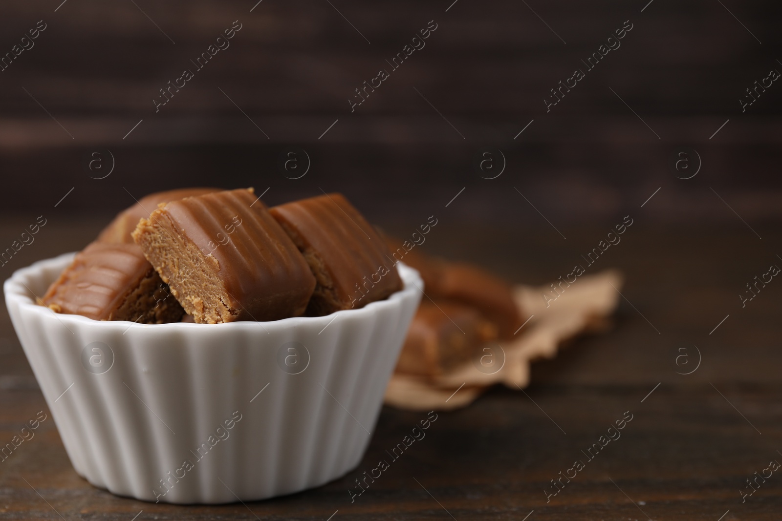 Photo of Tasty sweet caramel candies in bowl on wooden table, space for text