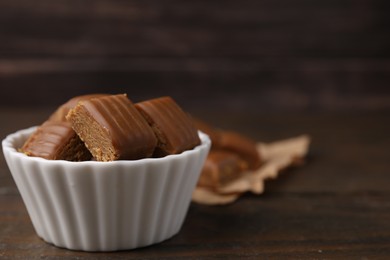 Photo of Tasty sweet caramel candies in bowl on wooden table, space for text