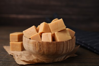 Photo of Tasty sweet caramel candies in bowl on wooden table