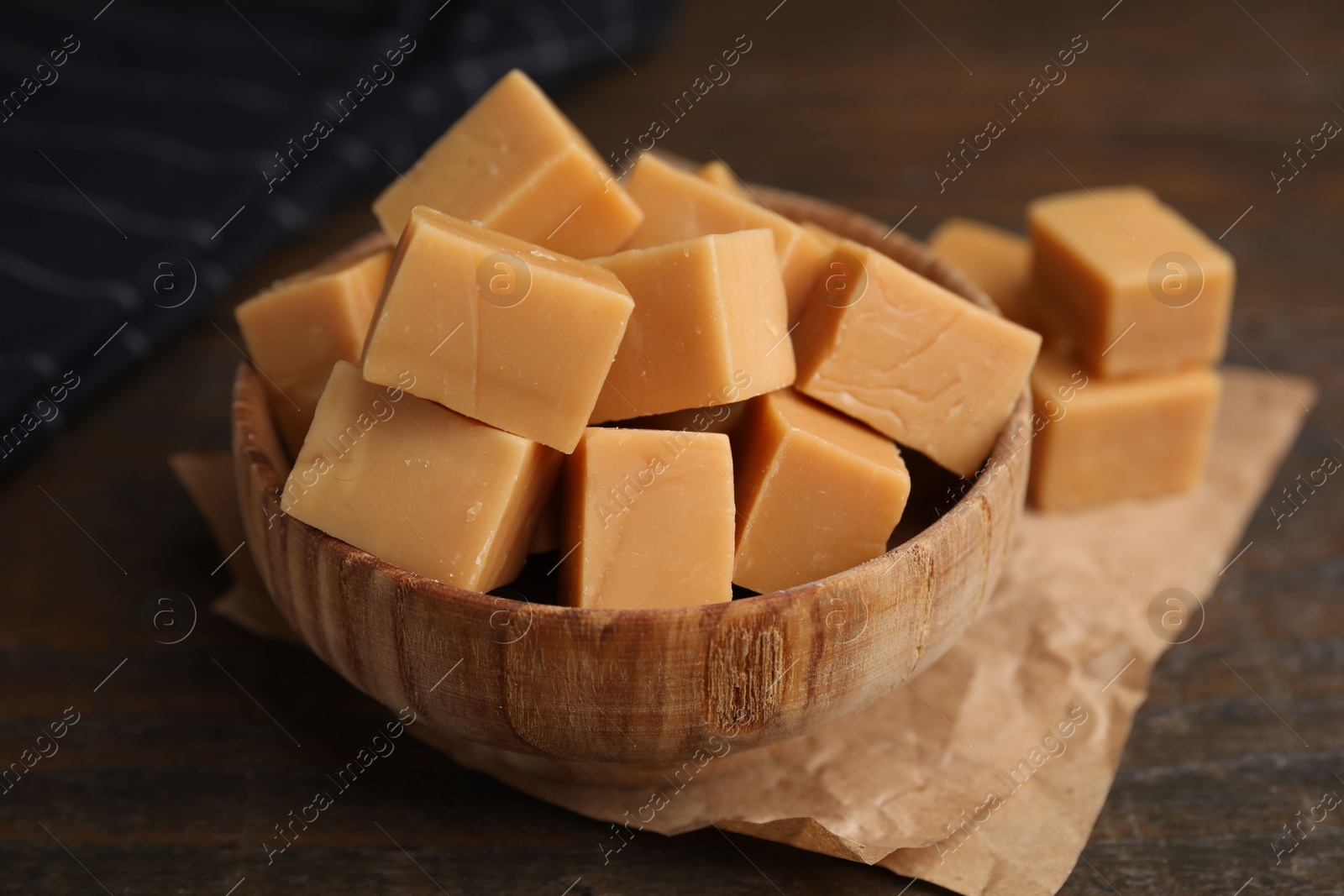 Photo of Tasty sweet caramel candies in bowl on wooden table, closeup