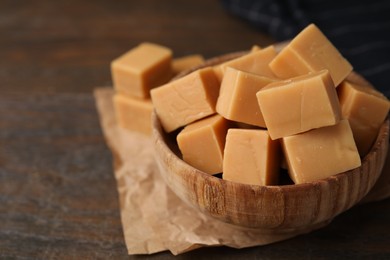 Photo of Tasty sweet caramel candies in bowl on wooden table, closeup. Space for text