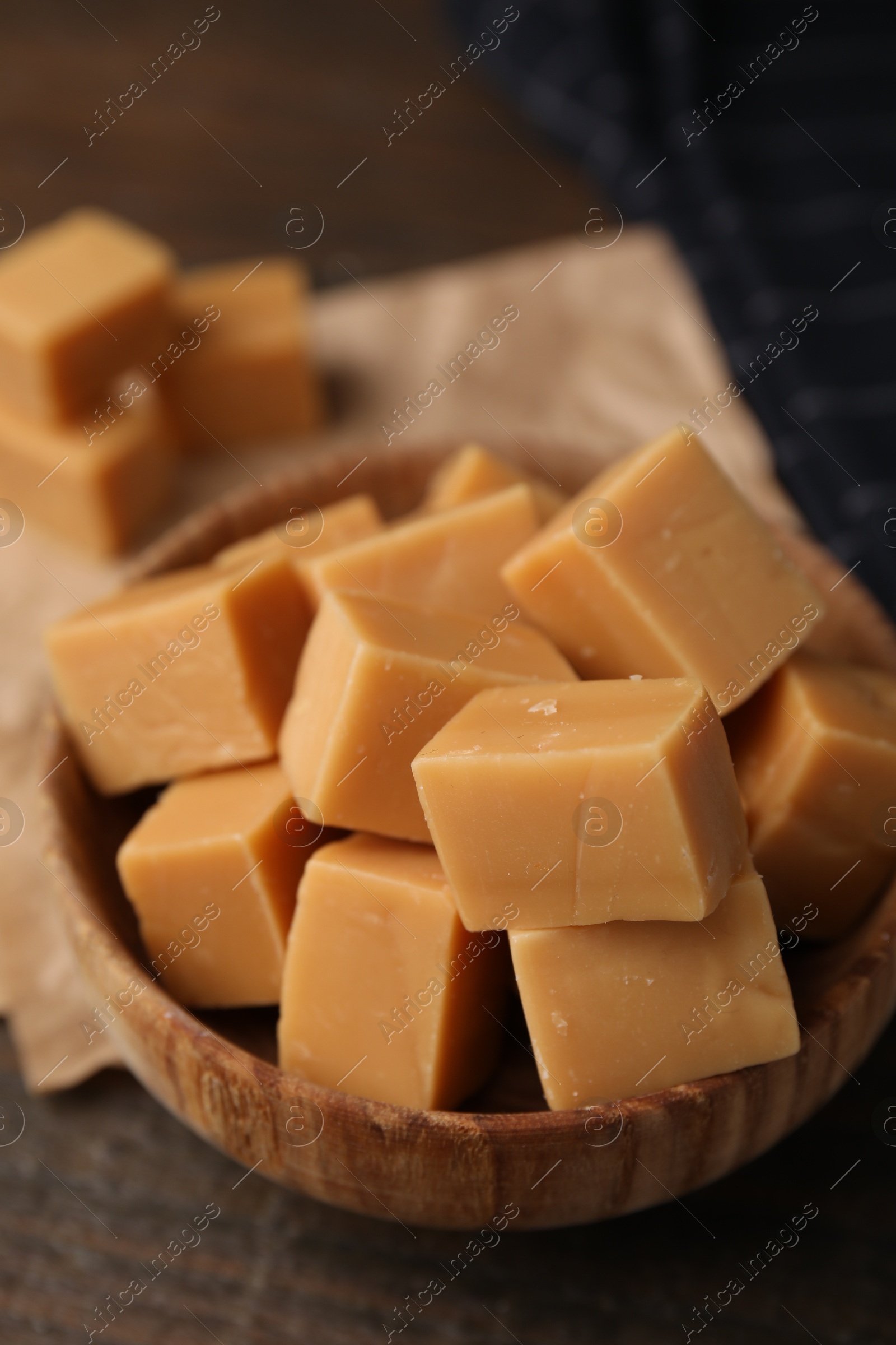 Photo of Tasty sweet caramel candies in bowl on wooden table, closeup