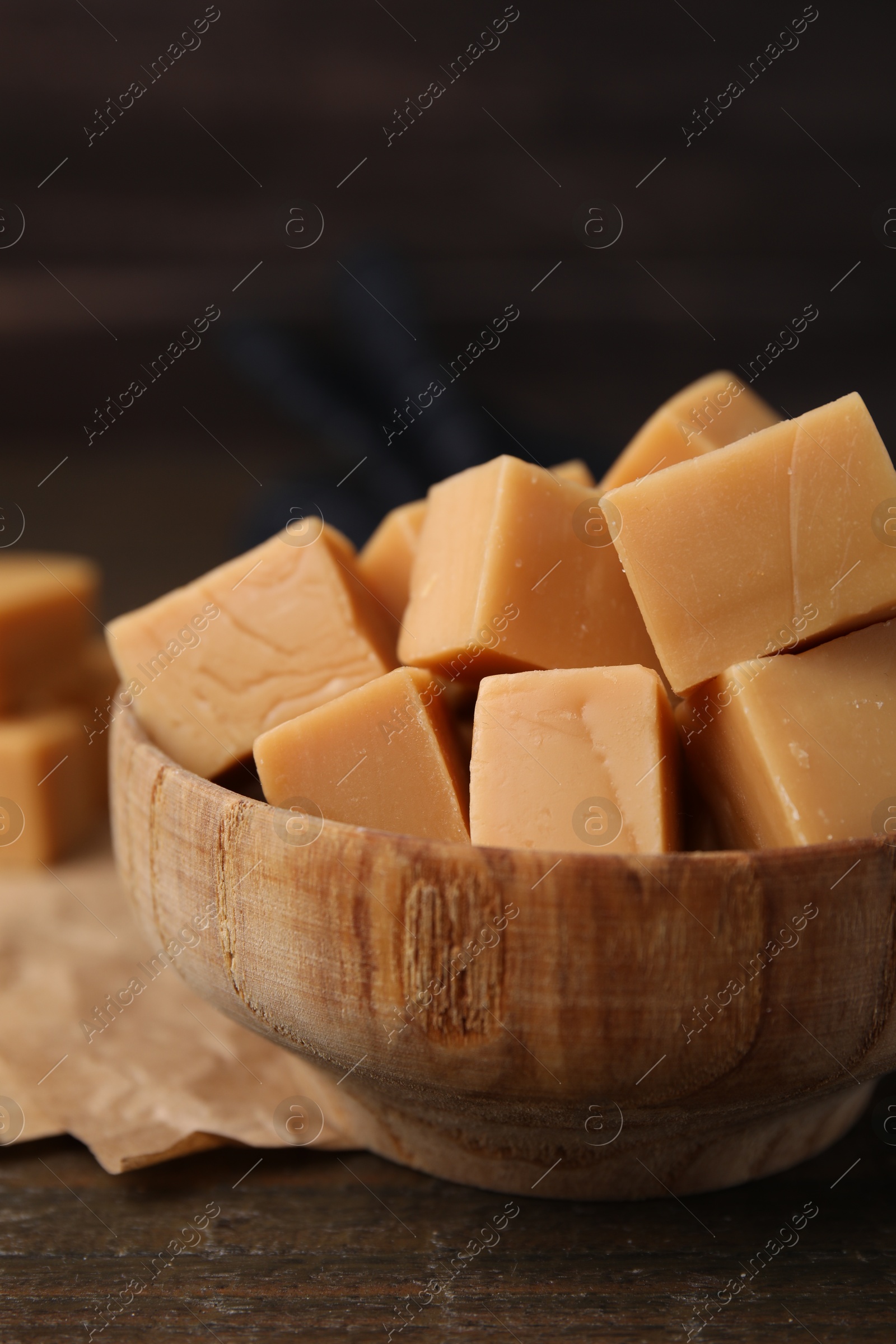 Photo of Tasty sweet caramel candies in bowl on wooden table, closeup