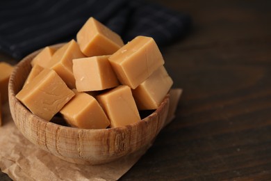 Photo of Tasty sweet caramel candies in bowl on wooden table, closeup. Space for text