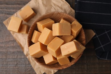 Photo of Tasty sweet caramel candies in bowl on wooden table, top view