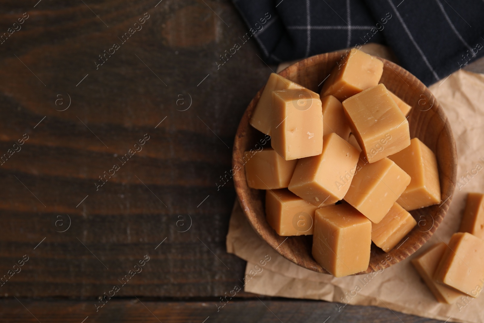 Photo of Tasty sweet caramel candies in bowl on wooden table, top view. Space for text