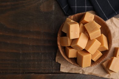 Photo of Tasty sweet caramel candies in bowl on wooden table, top view. Space for text