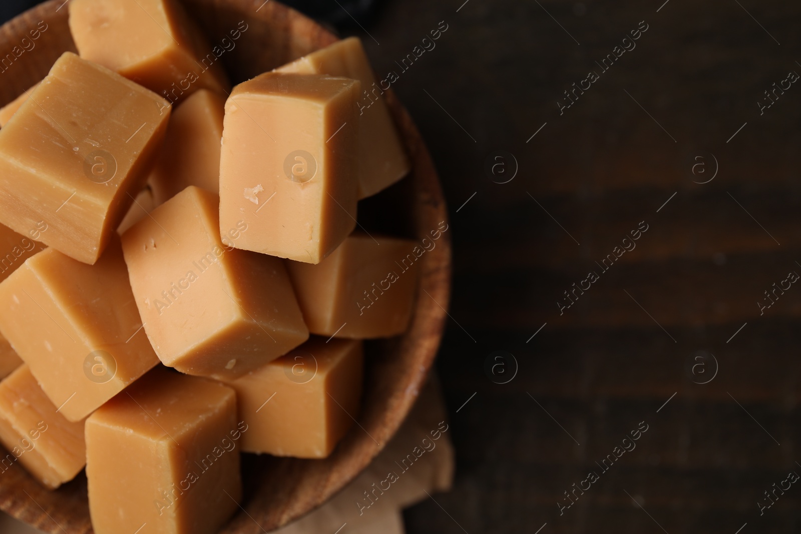 Photo of Tasty sweet caramel candies in bowl on wooden table, top view. Space for text