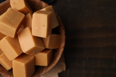 Photo of Tasty sweet caramel candies in bowl on wooden table, top view. Space for text