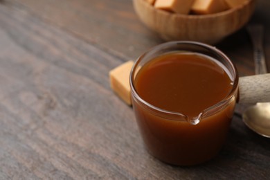 Photo of Tasty caramel sauce in glass measuring cup on wooden table, closeup. Space for text