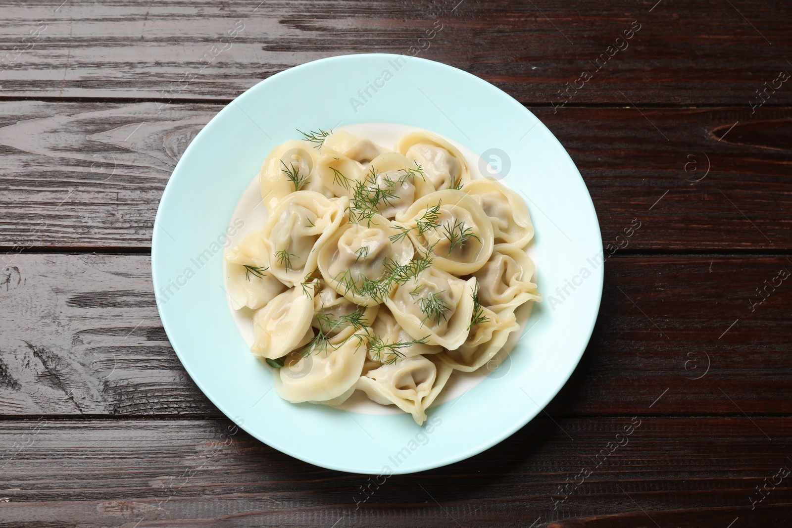 Photo of Delicious pelmeni with dill on wooden table, top view