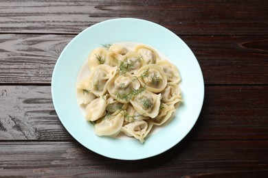 Photo of Delicious pelmeni with dill on wooden table, top view