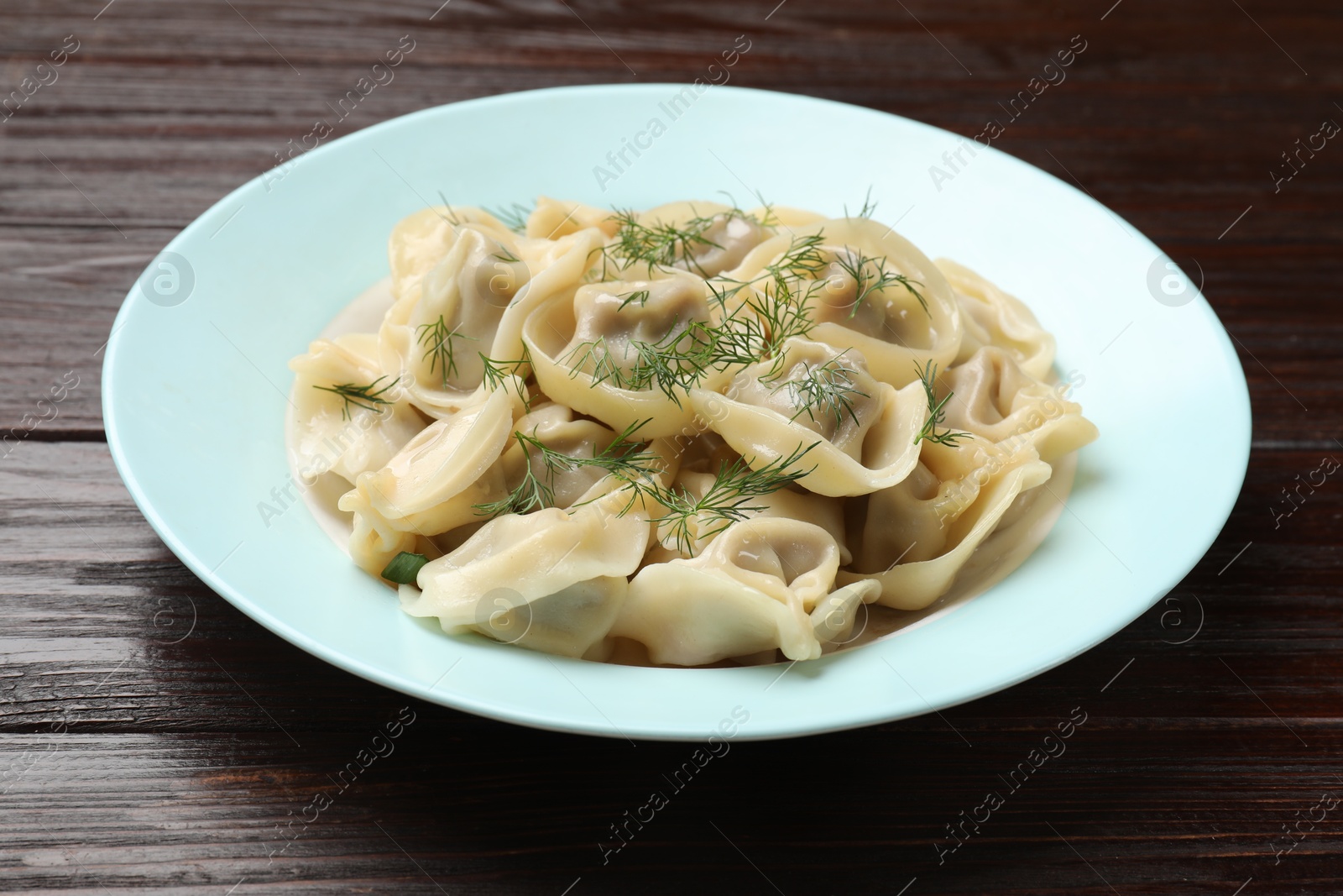 Photo of Delicious pelmeni with dill on wooden table