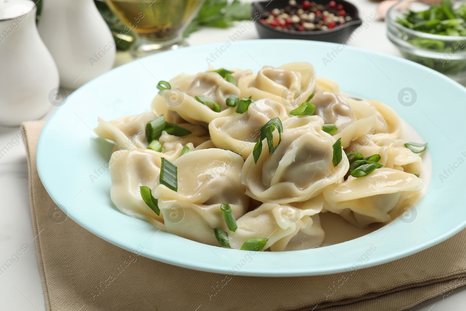 Photo of Delicious pelmeni with green onion served on white table, closeup