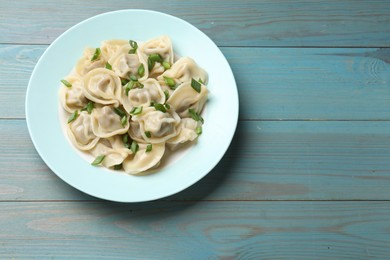 Photo of Delicious pelmeni with green onion on blue wooden table, top view. Space for text