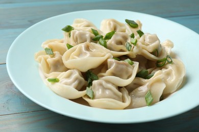 Photo of Delicious pelmeni with green onion on blue wooden table, closeup