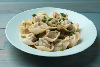 Photo of Delicious pelmeni with green onion on blue wooden table, closeup