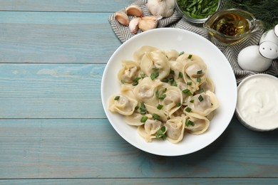 Photo of Delicious pelmeni with green onion served on blue wooden table, flat lay. Space for text